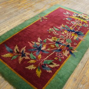 A magenta rug with a colorful botanical pattern and thick green border rests on distressed wooden planks.