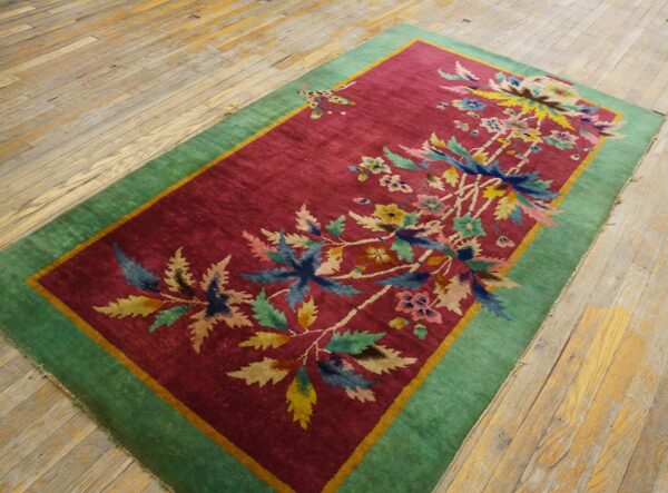 A magenta rug with a colorful botanical pattern and thick green border rests on distressed wooden planks.