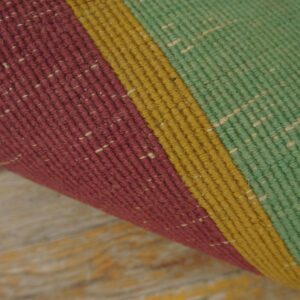 A rolled rug displaying thick vertical stripes of burgundy, mustard, and green rests on rustic wood planks.