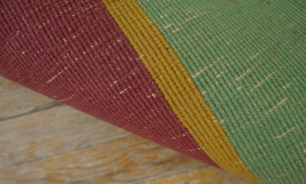 A rolled rug displaying thick vertical stripes of burgundy, mustard, and green rests on rustic wood planks.