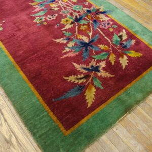 A magenta rug with a multicolored floral pattern and a wide green border rests on distressed wood planks.
