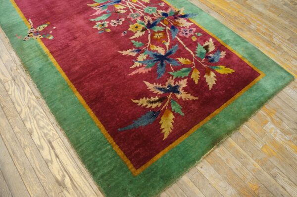 A magenta rug with a multicolored floral pattern and a wide green border rests on distressed wood planks.