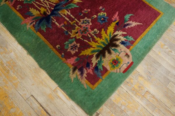 Magenta rug with floral vase design and teal border rests on distressed gray and yellow wooden planks.