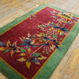 Multicolored floral rug with a cranberry field and green border rests on plank hardwood floors.