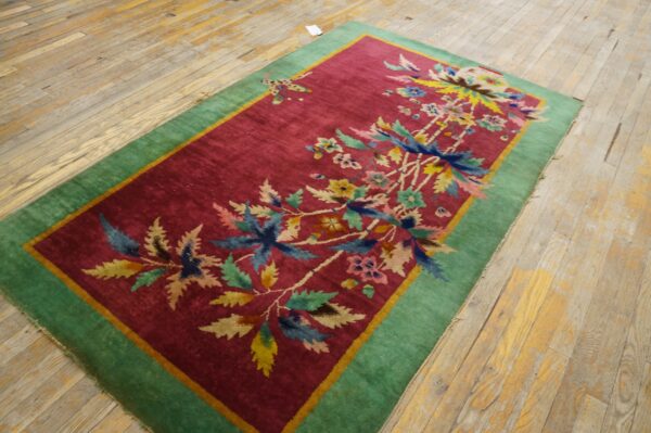 Multicolored floral rug with a cranberry field and green border rests on plank hardwood floors.