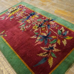 Magenta rug with a colorful floral and butterfly design, a green border, sitting on wood floor.