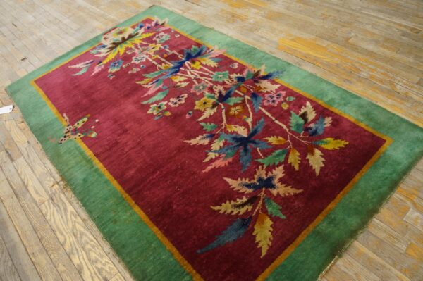 Magenta rug with a colorful floral and butterfly design, a green border, sitting on wood floor.