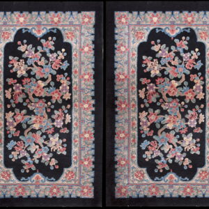 Matching pair of black rugs featuring a large, ornate floral design in dusty rose, blue, and lavender with thick borders.