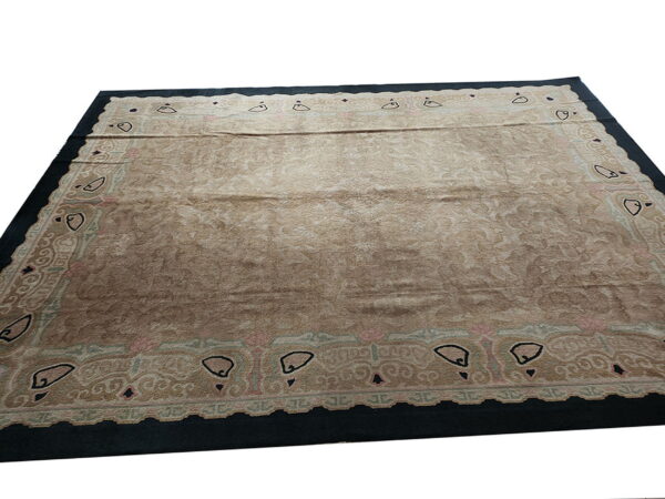 Tan rug featuring a subtle tone-on-tone floral pattern, framed by a dark border with stylized black motifs.