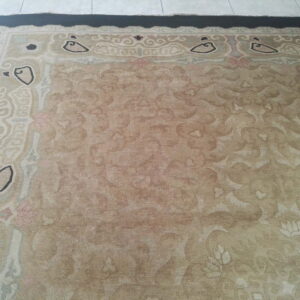 Faded beige low-pile rug with stylized cream, black, and pink borders rests on light tiled flooring.