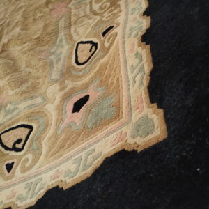 Close-up of a tan rug with pink, sage green, and black curvilinear patterns resting on dark flooring.