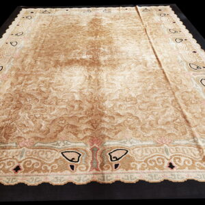 Distressed tan and brown rug with an elaborate border featuring black, pink, and green traditional motifs.