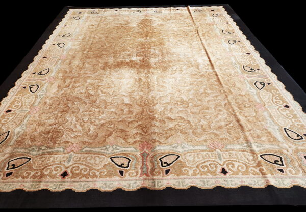 Distressed tan and brown rug with an elaborate border featuring black, pink, and green traditional motifs.