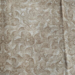 Close-up of a low-pile tan and beige rug featuring a distressed floral pattern with hints of pink and blue near the edge.