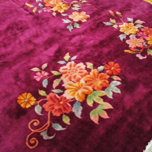 Plush magenta rug with orange and peach floral sprays lies over distressed light wood flooring.