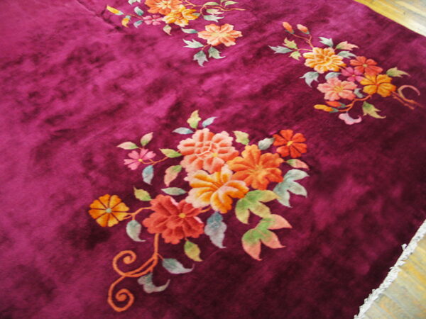 Plush magenta rug with orange and peach floral sprays lies over distressed light wood flooring.