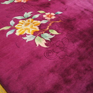 Deep magenta plush rug featuring carved yellow and pink flowers rests on hardwood flooring.