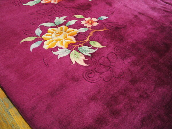 Deep magenta plush rug featuring carved yellow and pink flowers rests on hardwood flooring.