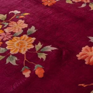 Crimson rug with a low pile texture and stylized floral patterns in peach, yellow, and green.
