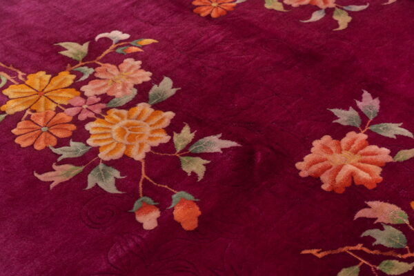 Crimson rug with a low pile texture and stylized floral patterns in peach, yellow, and green.