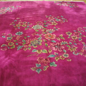 A plush magenta rug with scattered multicolor floral branches lays on a light wooden floor.