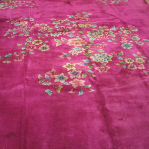 Deep magenta plush rug displays a sprawling floral pattern in blue, pink, and green on wood floors.