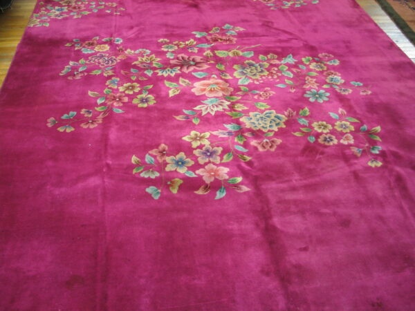 Deep magenta plush rug displays a sprawling floral pattern in blue, pink, and green on wood floors.