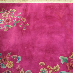 Fuchsia pile rug featuring multicolor floral sprigs along the borders, with fringe visible on wood flooring.