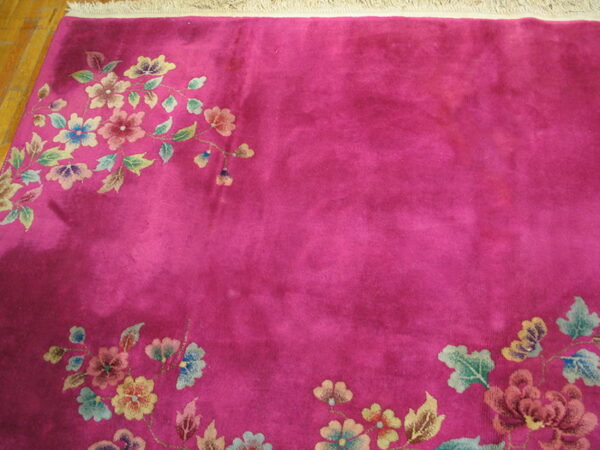 Fuchsia pile rug featuring multicolor floral sprigs along the borders, with fringe visible on wood flooring.