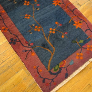Deep blue floral runner with a rust border sits on worn, diagonally-laid golden wood planks.