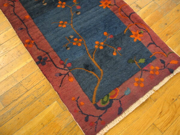Deep blue floral runner with a rust border sits on worn, diagonally-laid golden wood planks.