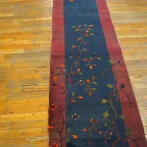 Dark blue runner rug with colorful floral vines and red borders rests on worn wood floors.