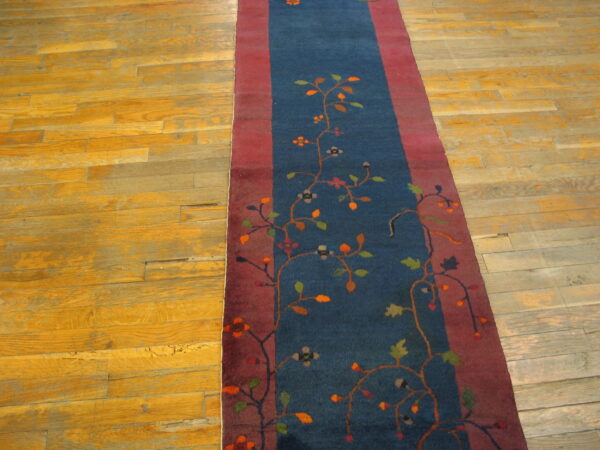 Dark blue runner rug with colorful floral vines and red borders rests on worn wood floors.