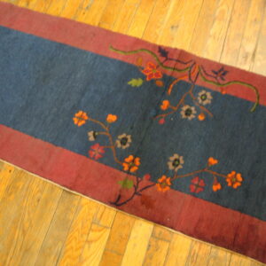 Dark blue runner featuring orange and beige floral patterns within red borders on shiny light wood flooring.