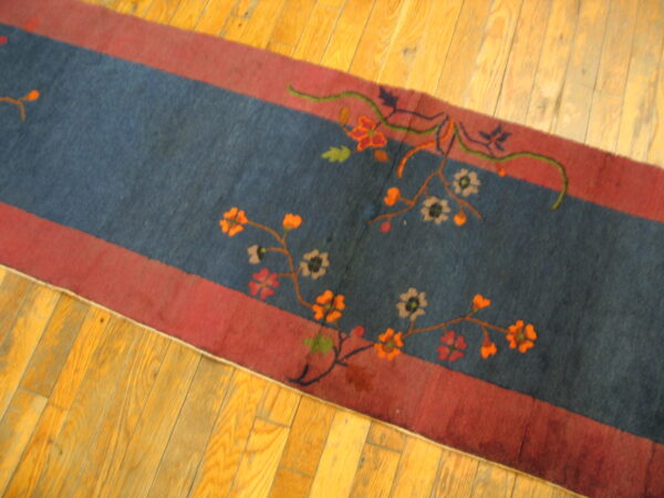 Dark blue runner featuring orange and beige floral patterns within red borders on shiny light wood flooring.