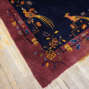 Deep navy and burgundy rug featuring colorful birds and floral motifs rests on light, heavily distressed wood flooring.