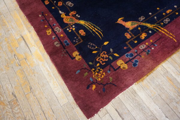 Deep navy and burgundy rug featuring colorful birds and floral motifs rests on light, heavily distressed wood flooring.