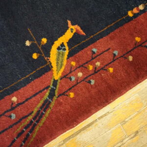 Stylized yellow bird pattern on a dark rug border transitions to maroon, lying on distressed wood floor.