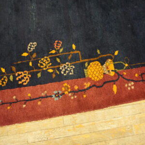 Navy and rust rug border features a detailed floral vine pattern on light distressed wood planks.