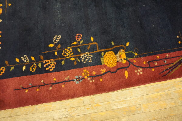 Navy and rust rug border features a detailed floral vine pattern on light distressed wood planks.