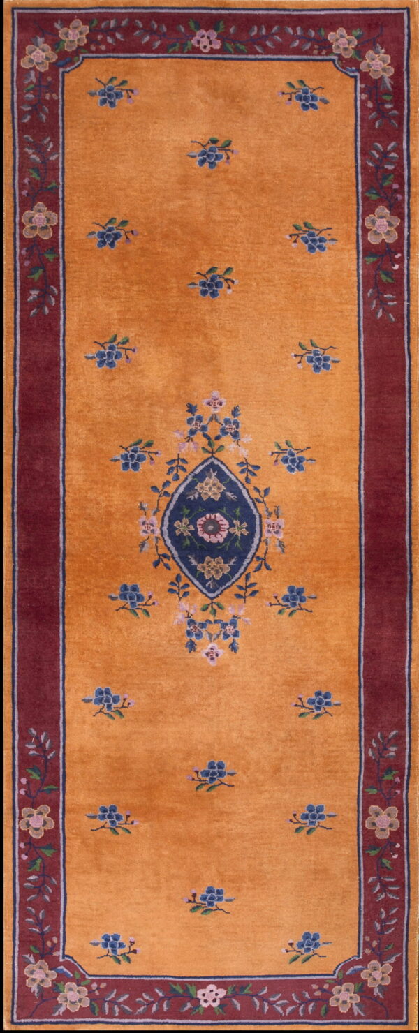 Orange runner rug with a central blue floral medallion, scattered blue motifs, and a wide maroon border.