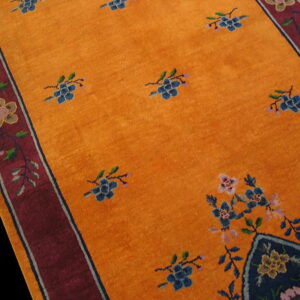 Orange rug with blue floral sprays, a wide red border, and a dark blue corner medallion.