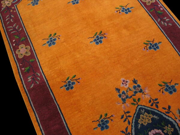 Orange rug with blue floral sprays, a wide red border, and a dark blue corner medallion.