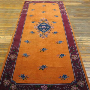 Long orange runner rug with a central blue medallion and burgundy floral border on plank wood floors.