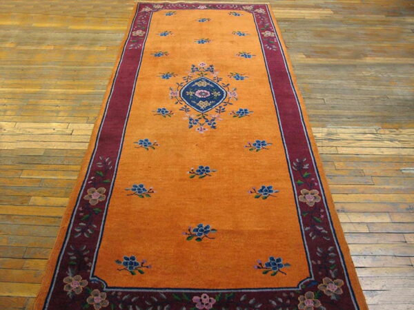 Long orange runner rug with a central blue medallion and burgundy floral border on plank wood floors.