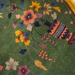 Medium-pile green rug features a colorful floral and vine pattern with a vase and yellow border.