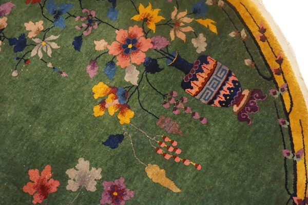 Medium-pile green rug features a colorful floral and vine pattern with a vase and yellow border.