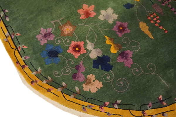 Lush green rug pile detail showing multi-colored flowers, winding vines, and a mustard yellow border.