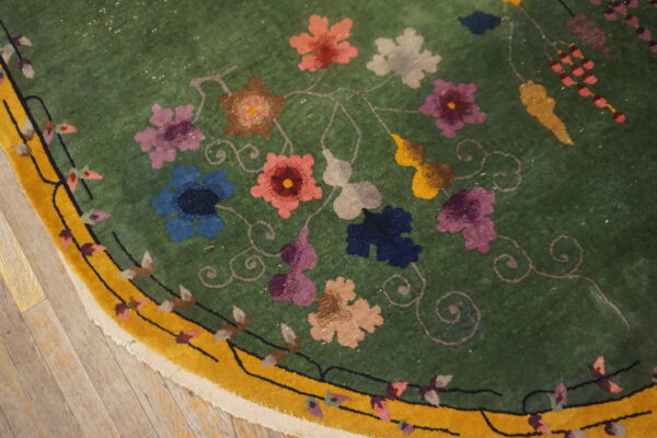 Green rug with colorful floral and vine patterns bordered by bright yellow rests on wood planks.