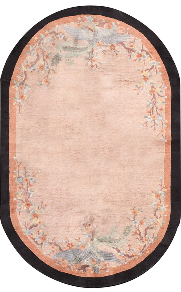 Oval pink rug featuring a floral and bird pattern border with terracotta and black edges.